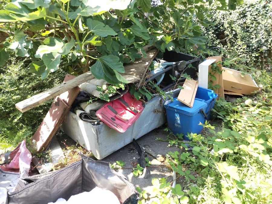 Fly-tipped waste dumped in undergrowth beside a wall