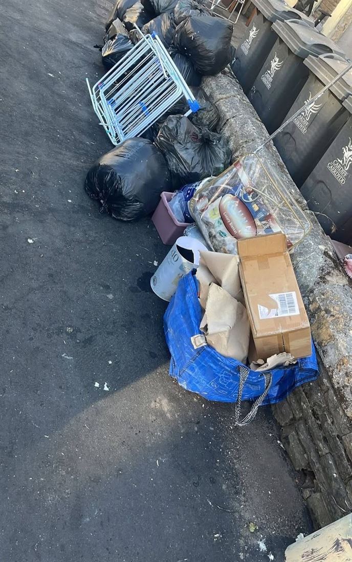 Rubbish bags, boxes and a bed frame dumped along a Cardiff back lane beside council bins